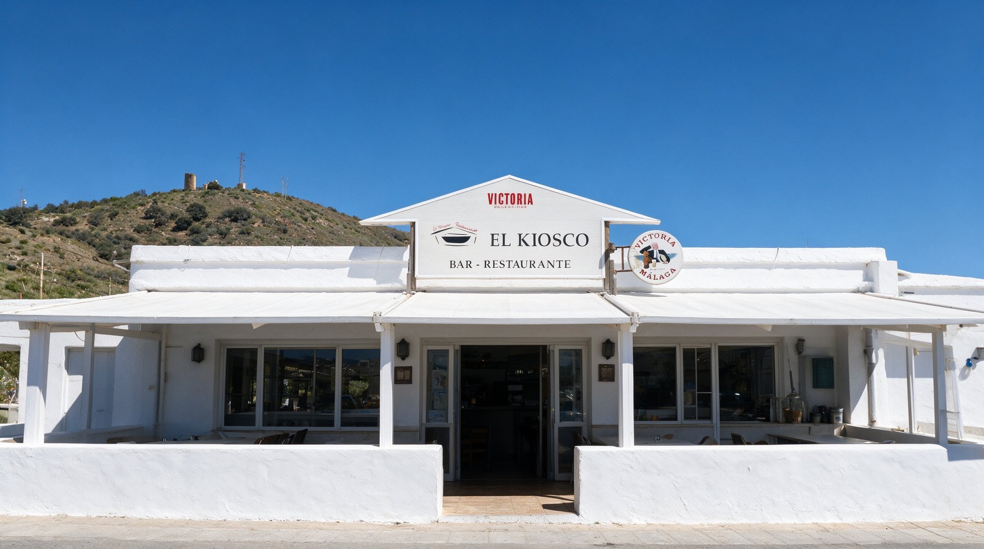 Fachada de Restaurante Kiosco Lagos, chiringuito con el rótulo EL KIOSCO en rojo y el mar de fondo